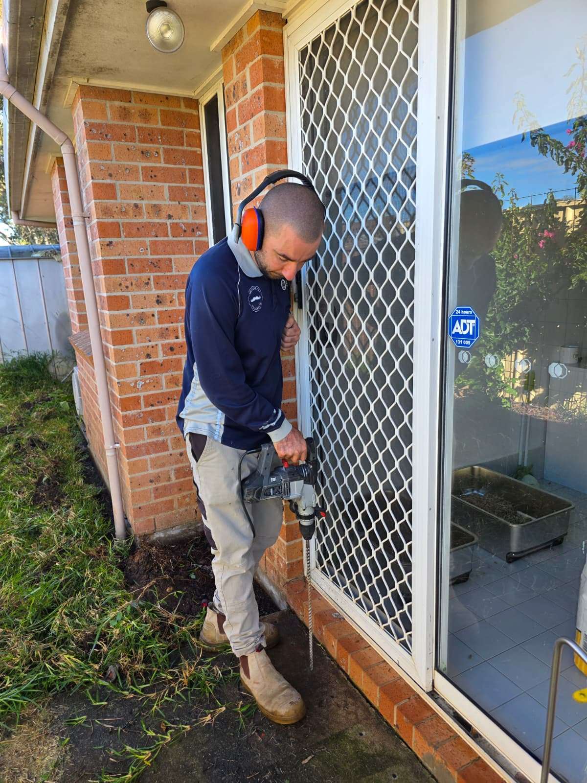 OCG Pest Control technician drilling a termite barrier beside a doorway